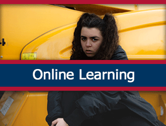 A scared student sitting by a yellow construction machine. A ribbon that says 