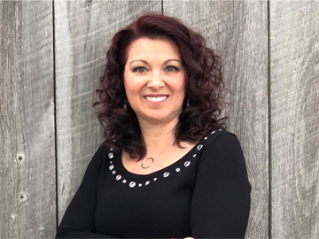 Shannon Robinson, SHRM instructor, smiles and stands in front of a wood-plank wall