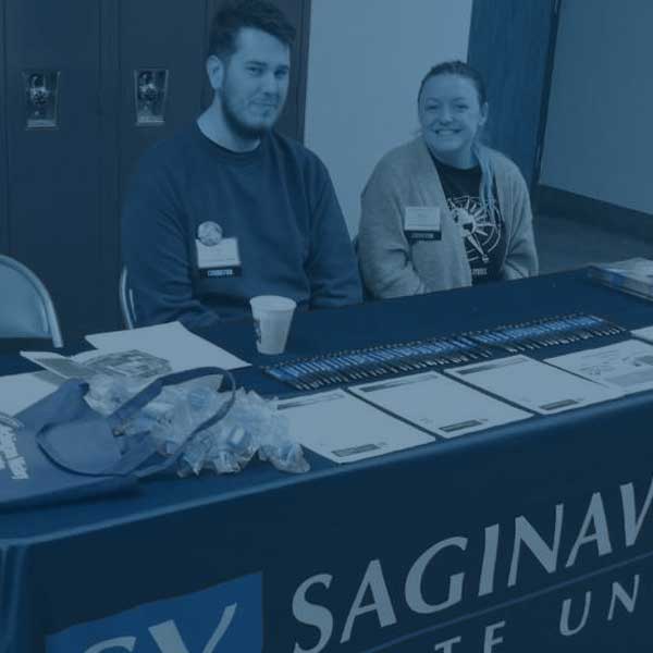 Students set up at table in a school to promote svsu history programs