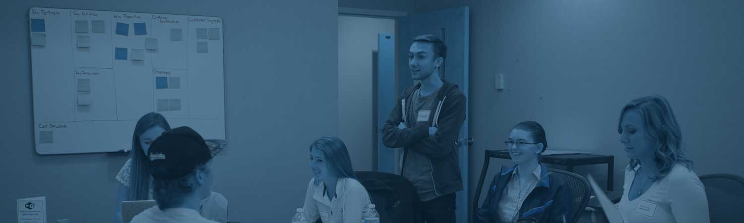 Students having a discussion around a table with a whiteboard in the background