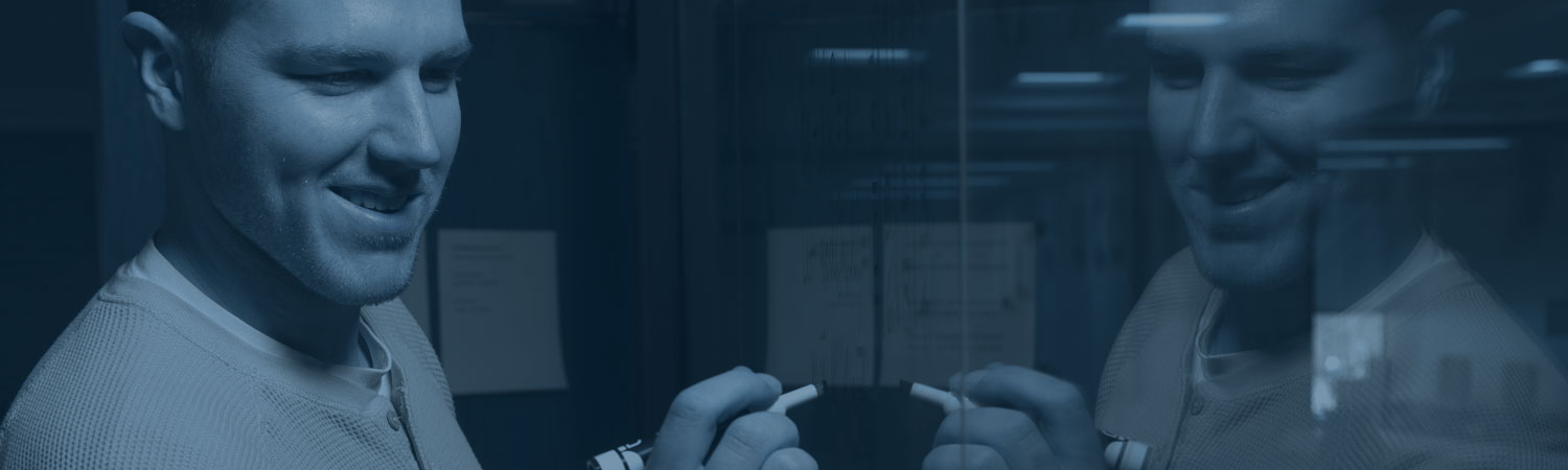 Student writing on a board, with his image reflected