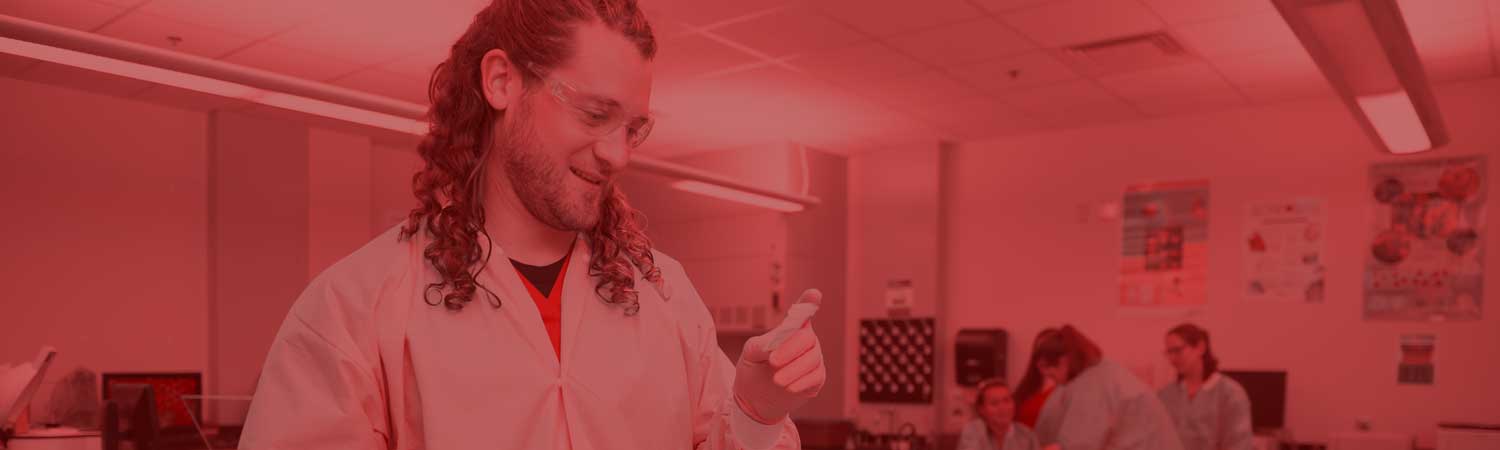 student in lab coat and goggles working in a lab