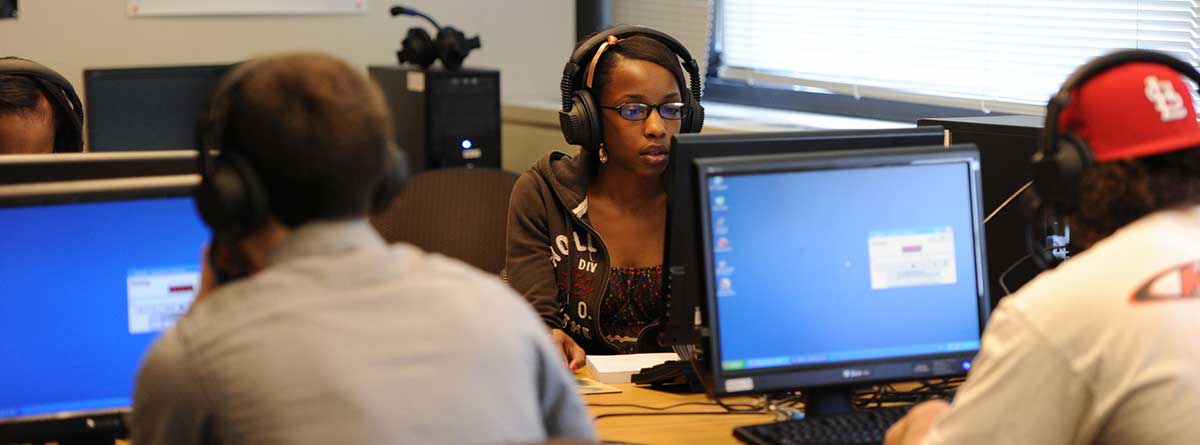 Language lab with computers and three students each at a computer. The lab is designed to enhance student listening, speaking, writing and reading skills. 