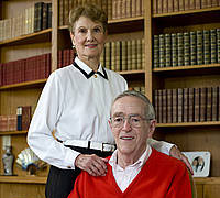 A woman standing behind a man seated in a library